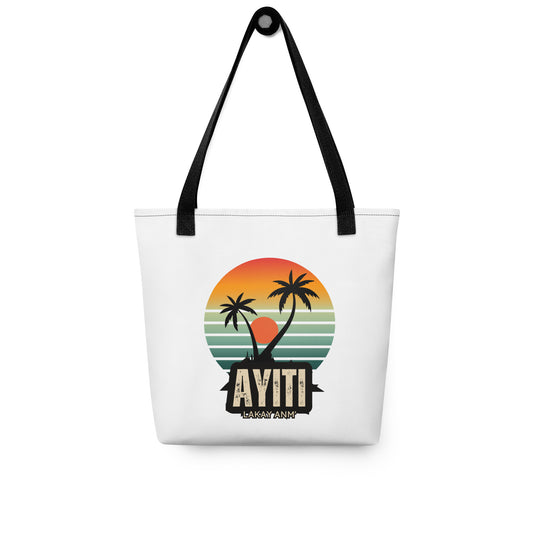 White canvas tote bag with black handles, featuring a circular graphic with an orange and yellow sunset over blue and green stripes, silhouetted by two palm trees. The text 'AYITI' and 'LAKAY ANM'' is below the graphic in a stylized font.