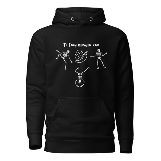 A black pullover hoodie with a white line-art graphic of three dancing skeletons. The middle skeleton is doing a handstand. Above them is a hot pepper with flames, and the text 'TI TOUY BEZWEN NAN'. The design is a playful nod to a Haitian cultural tradition.