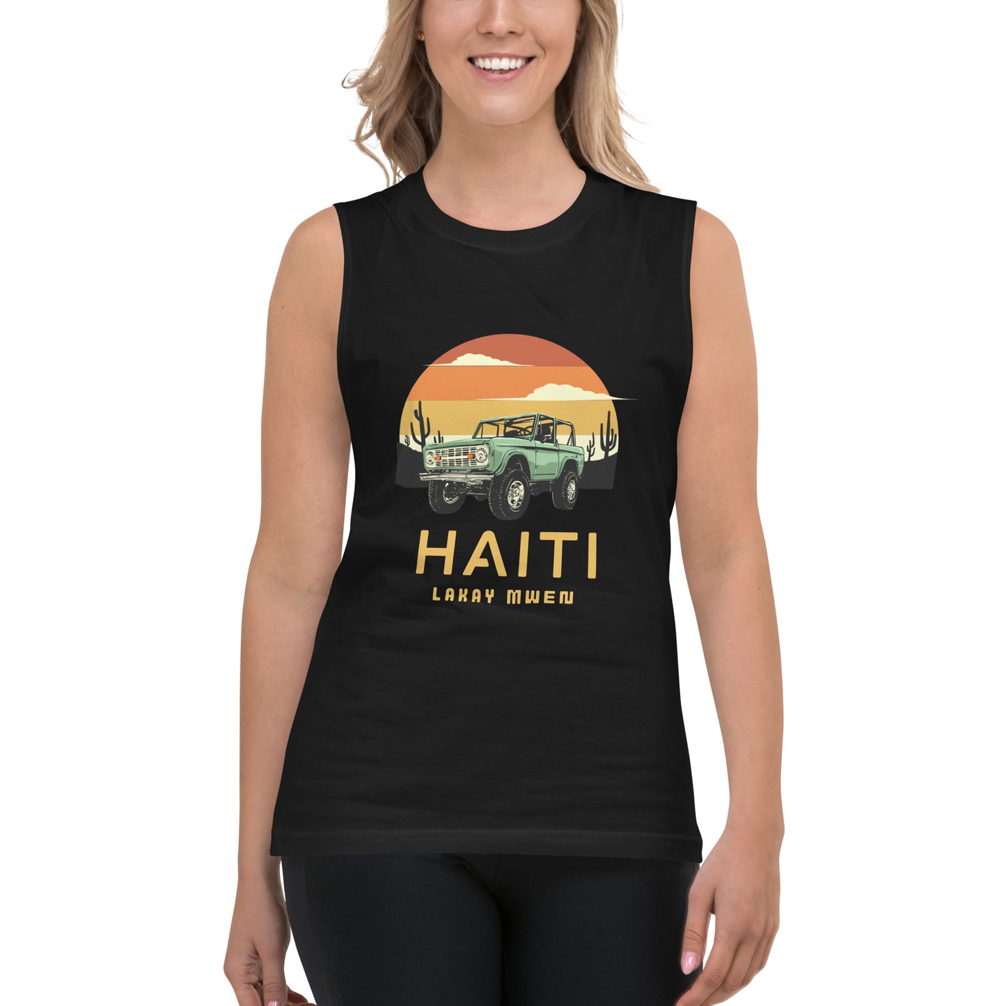 Smiling white female model standing wearing a black Bella+Canvas 'HAITI LAKAY MWEN' unisex muscle tank top (front view) featuring a retro sunset and green vintage Jeep graphic. White background.