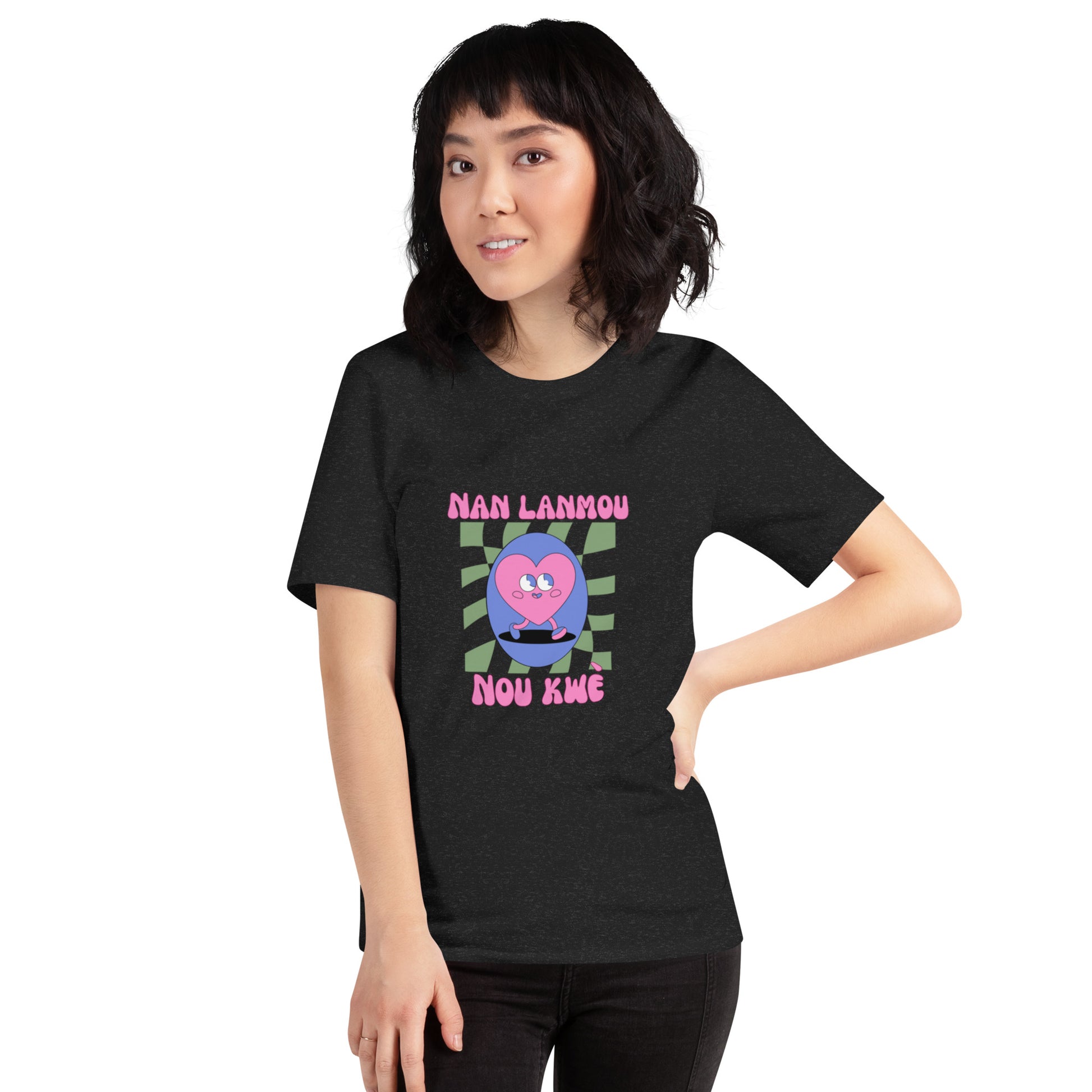 Asian woman wearing a black Bella+Canvas 'Nan Lanmou Nou Kwe' unisex T-shirt (front view) featuring a pink and blue abstract heart graphic with a smiley face and paint drip accents.
