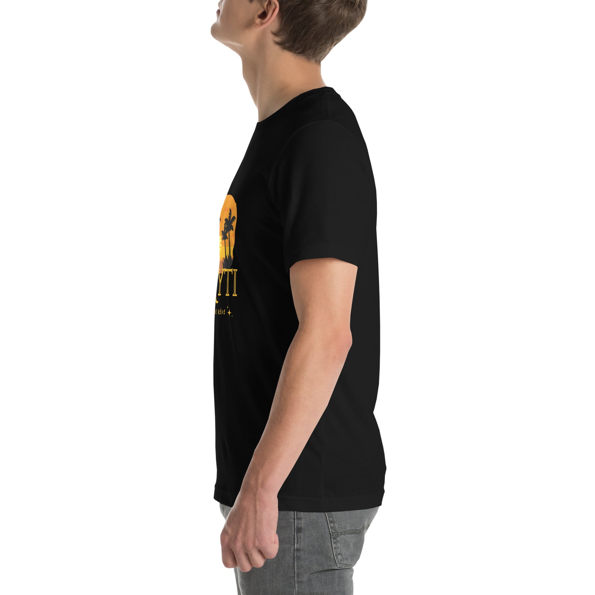 A white man wearing a black Bella+Canvas 'HAYTI PAYS DE RÊVE' unisex T-shirt (left side view) featuring a golden hour sunset graphic with palm trees and twinkling stars. White background.