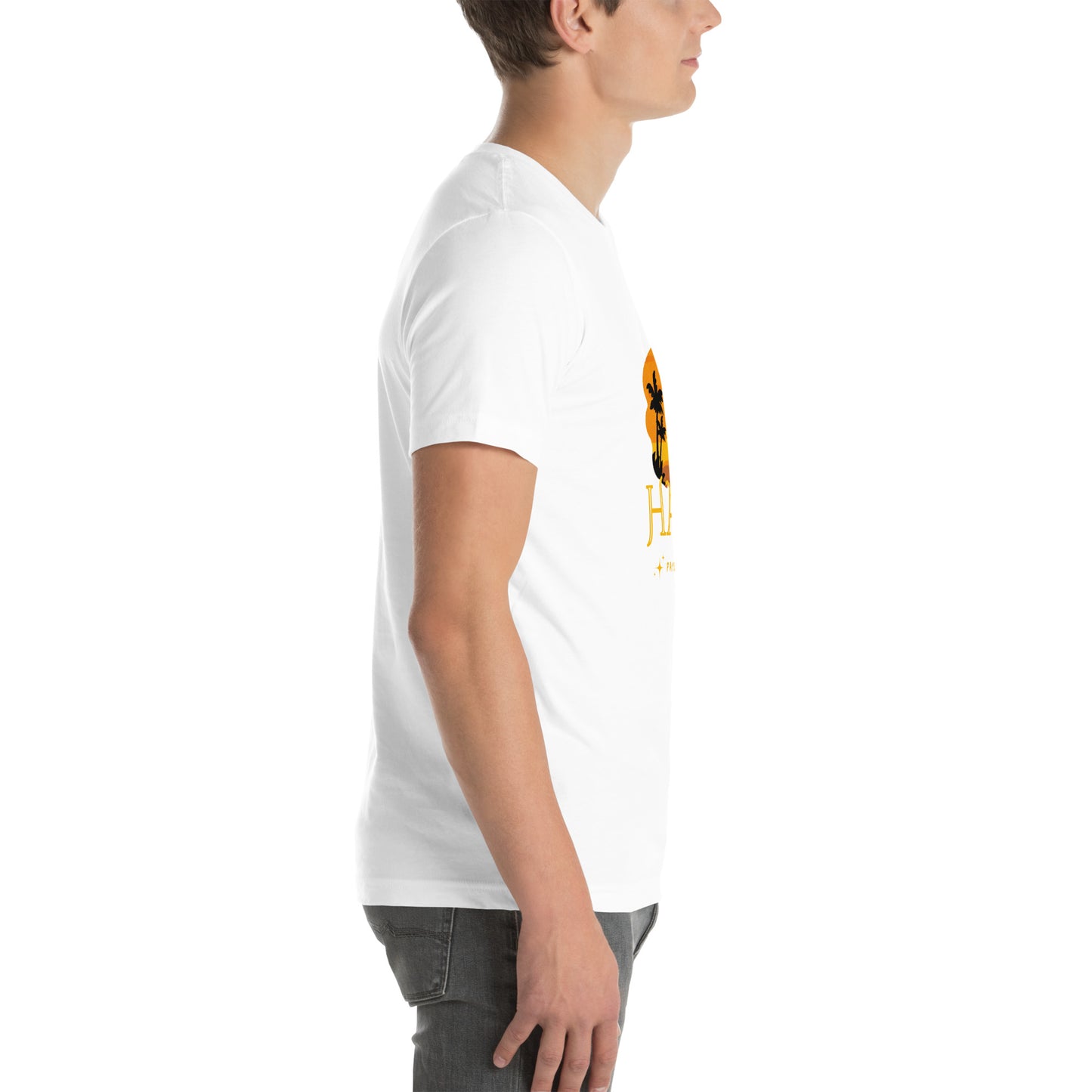 A white man wearing a white Bella+Canvas 'HAYTI PAYS DE RÊVE' unisex T-shirt (right side view) featuring a golden hour sunset graphic with palm trees and twinkling stars. White background.