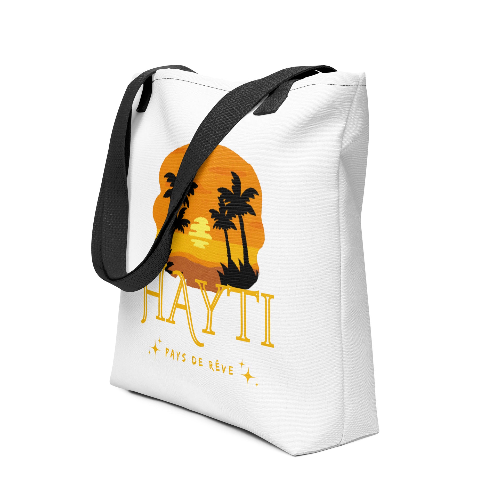 White canvas tote bag with black handles(left side view), featuring a golden and orange sunset graphic with silhouetted palm trees and the text 'HAYTI' and 'PAYS DE RÊVE' with small starburst accents.