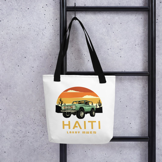 White canvas tote bag with black handles, featuring a circular orange and yellow sunset graphic with a green vintage Jeep, black mountains, and cactus silhouettes. The text 'HAITI' is below the graphic, with 'LAKAY MWEN' underneath it.
