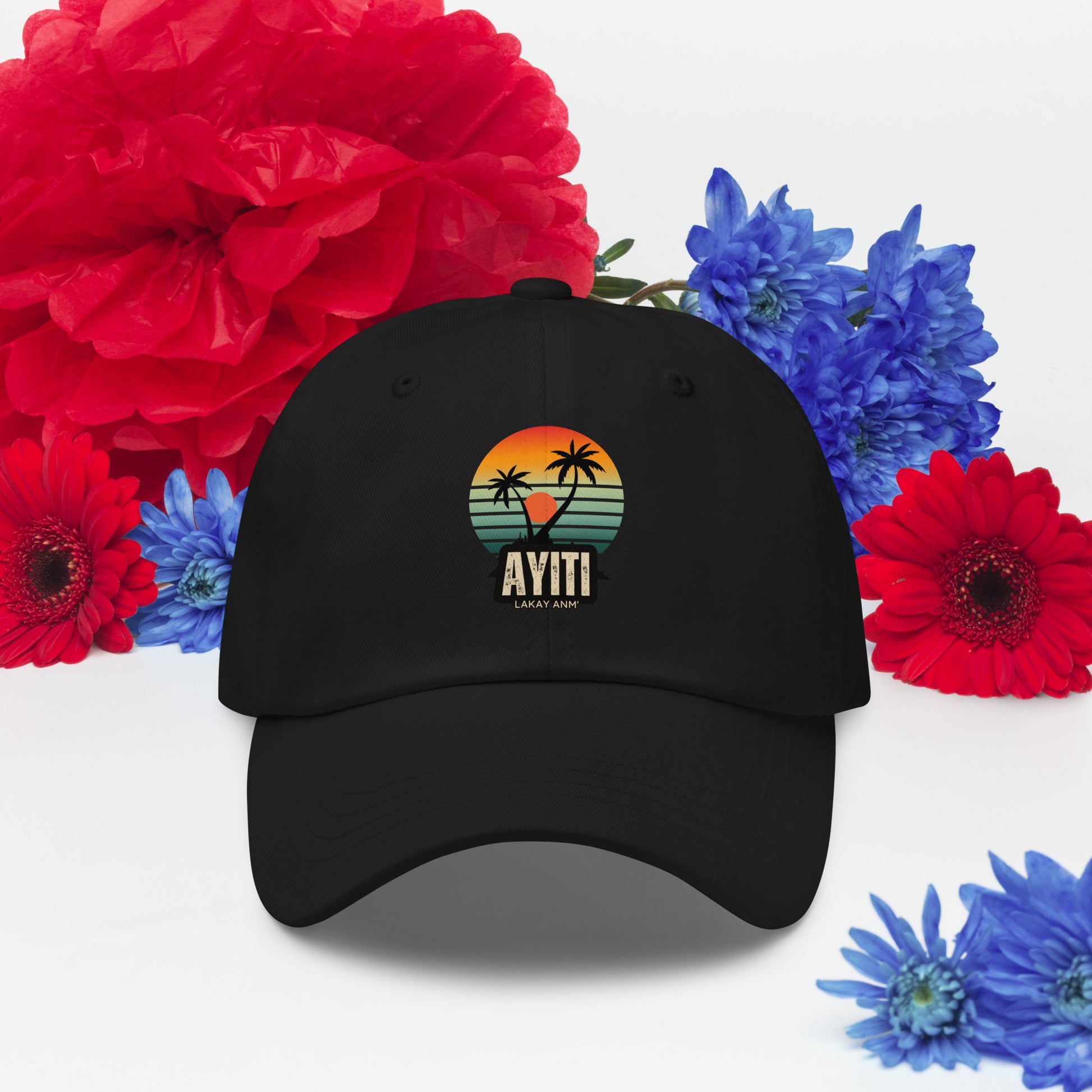Black baseball cap with a circular graphic on the front featuring an orange and yellow sunset over blue and green stripes, silhouetted by two palm trees. The text 'AYITI' and 'LAKAY ANM'' is below the graphic in a stylized font.