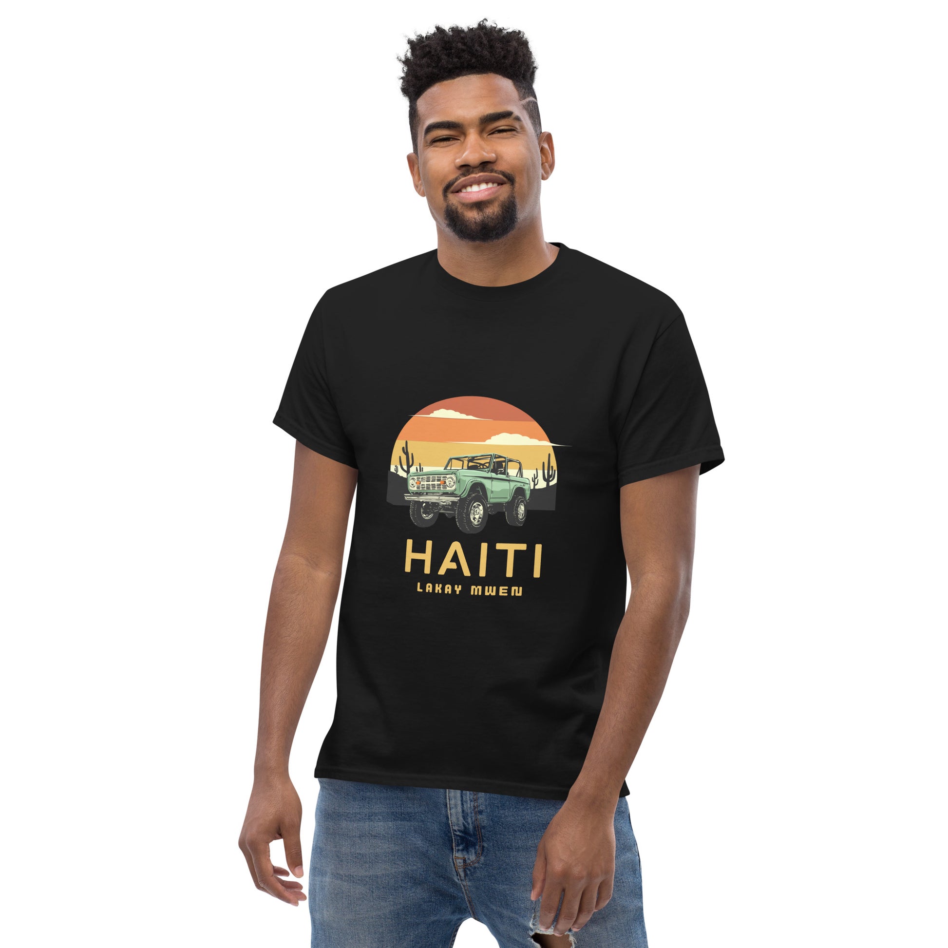 Black man standing and smiling wearing a Bella+Canvas 'Haiti Lakay Mwen' unisex T-shirt featuring a retro sunset and green vintage Jeep graphic. White background.