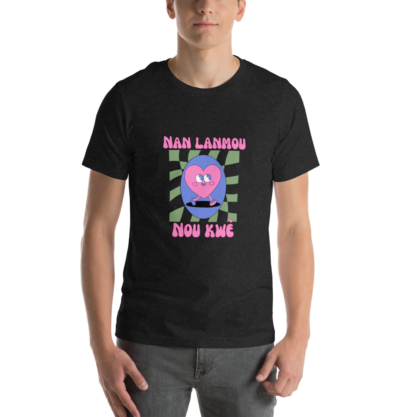 White man wearing a black Bella+Canvas 'Nan Lanmou Nou Kwe' unisex T-shirt (front view) featuring a pink and blue abstract heart graphic with a smiley face and paint drip accents.