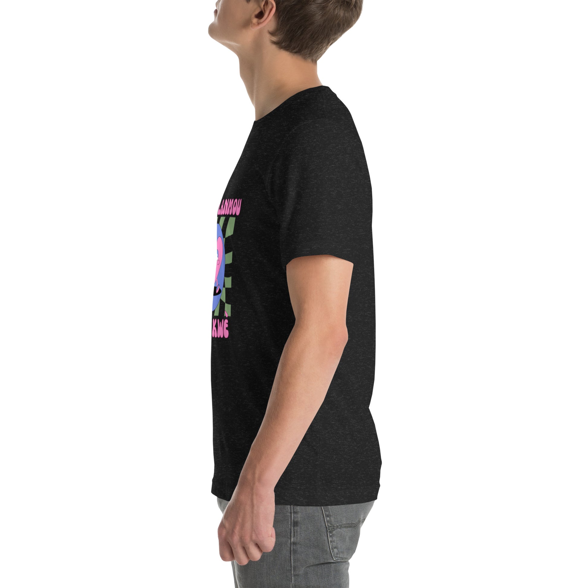 White man wearing a black Bella+Canvas 'Nan Lanmou Nou Kwe' unisex T-shirt (left side view) featuring a pink and blue abstract heart graphic with a smiley face and paint drip accents.