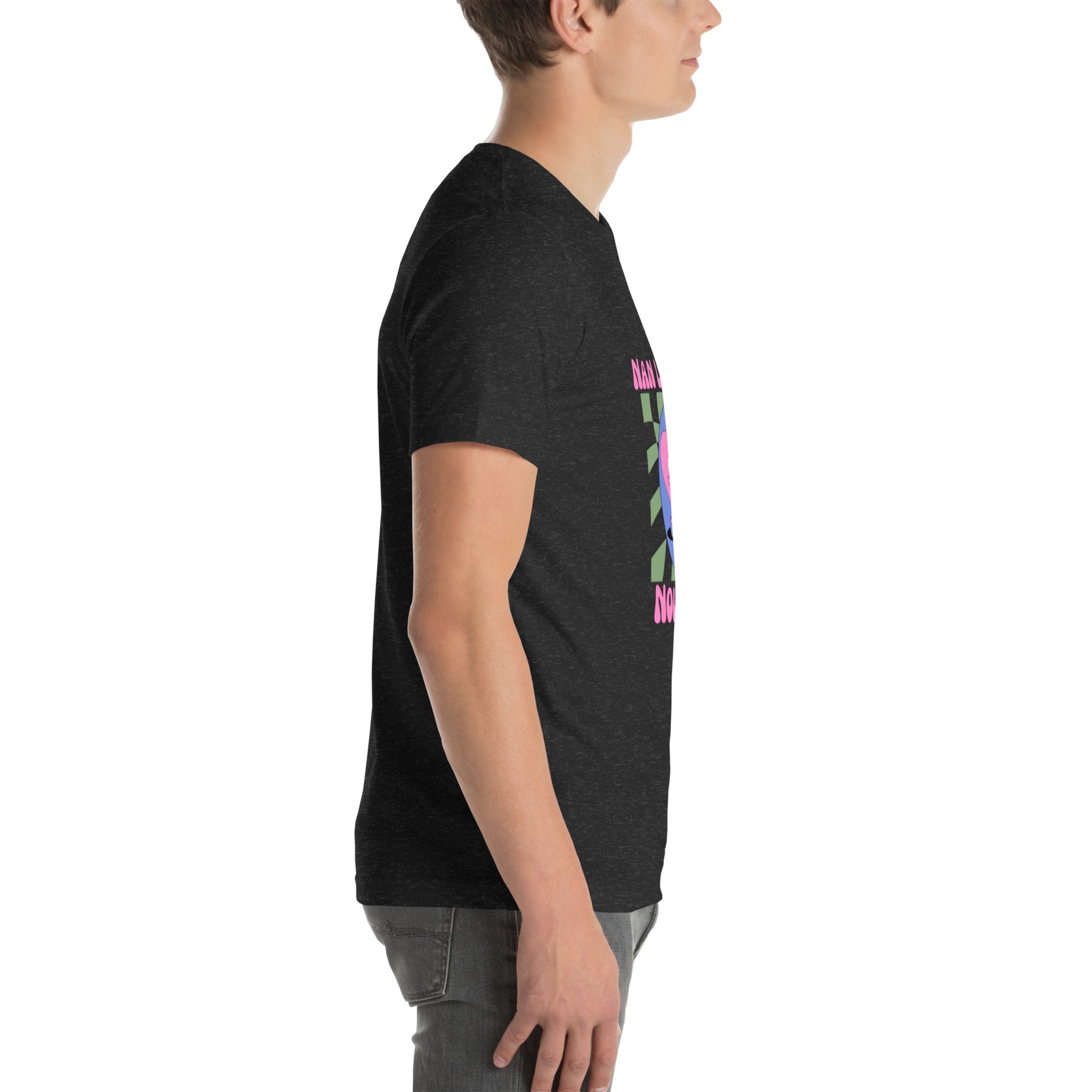 White man wearing a black Bella+Canvas 'Nan Lanmou Nou Kwe' unisex T-shirt (right side view) featuring a pink and blue abstract heart graphic with a smiley face and paint drip accents.
