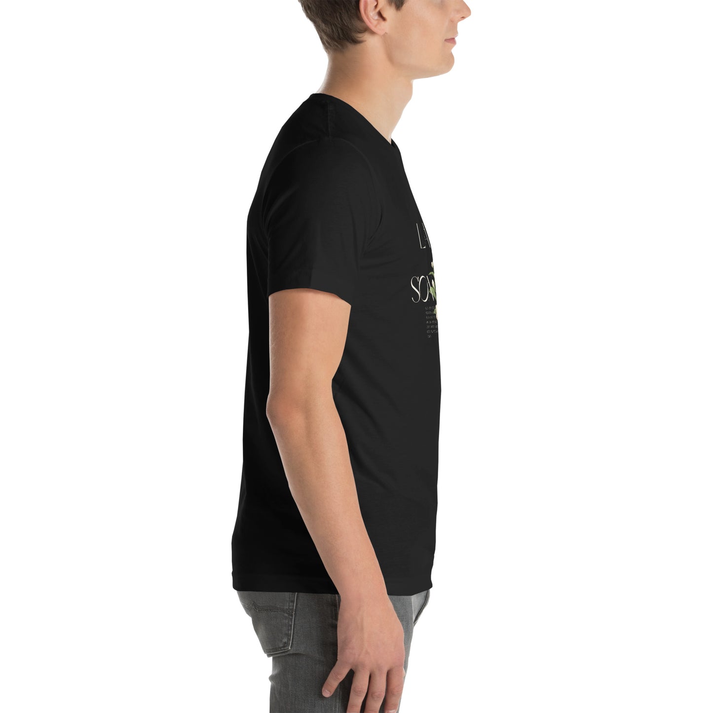 White Male model wearing a black Bella+Canvas 'LAVI S'ON BÈL RANS' unisex T-shirt (right side view) featuring cream text and a realistic white floral graphic