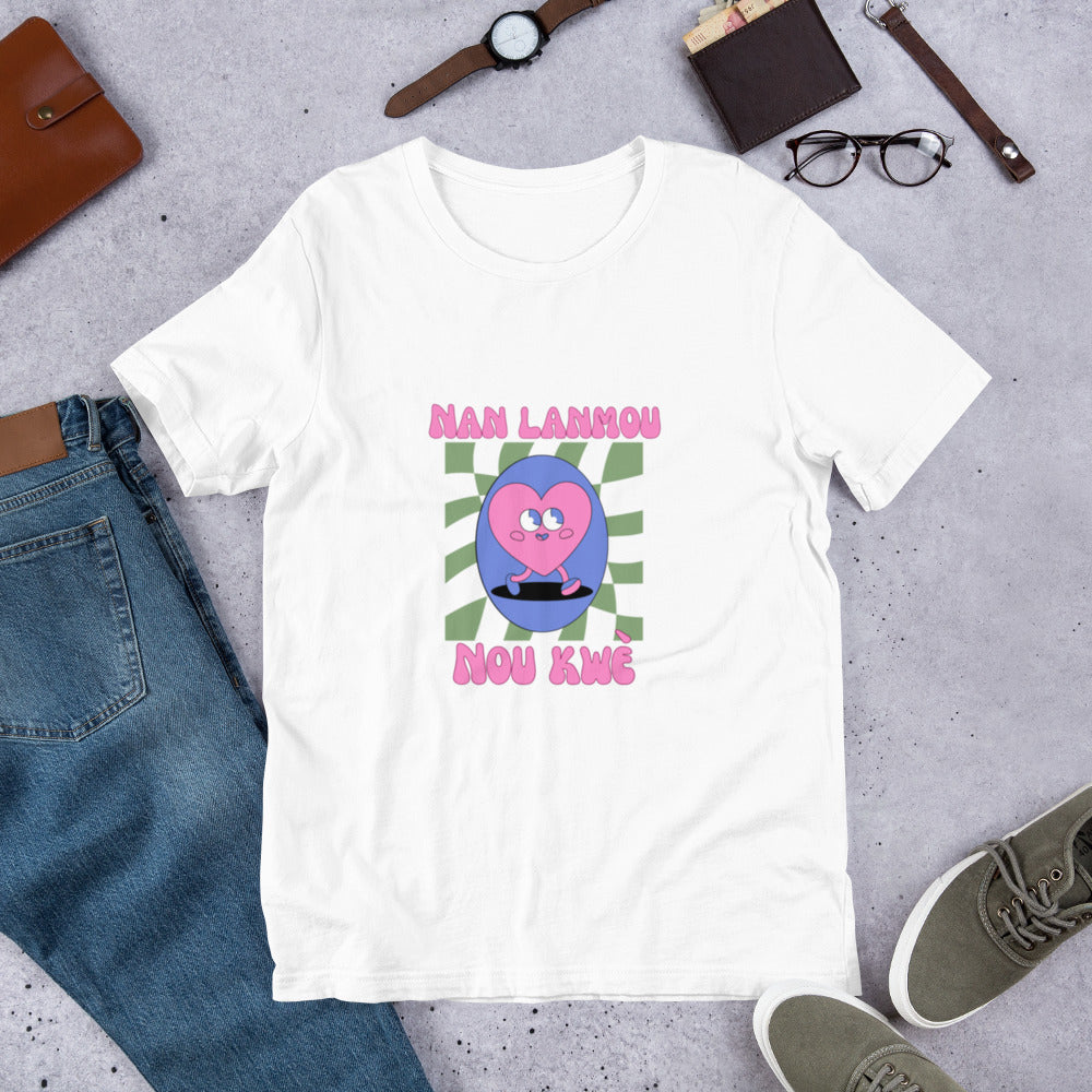 White Bella+Canvas 'Nan Lanmou Nou Kwe' unisex T-shirt (front view) featuring a pink and blue abstract heart graphic with a smiley face and paint drip accents.