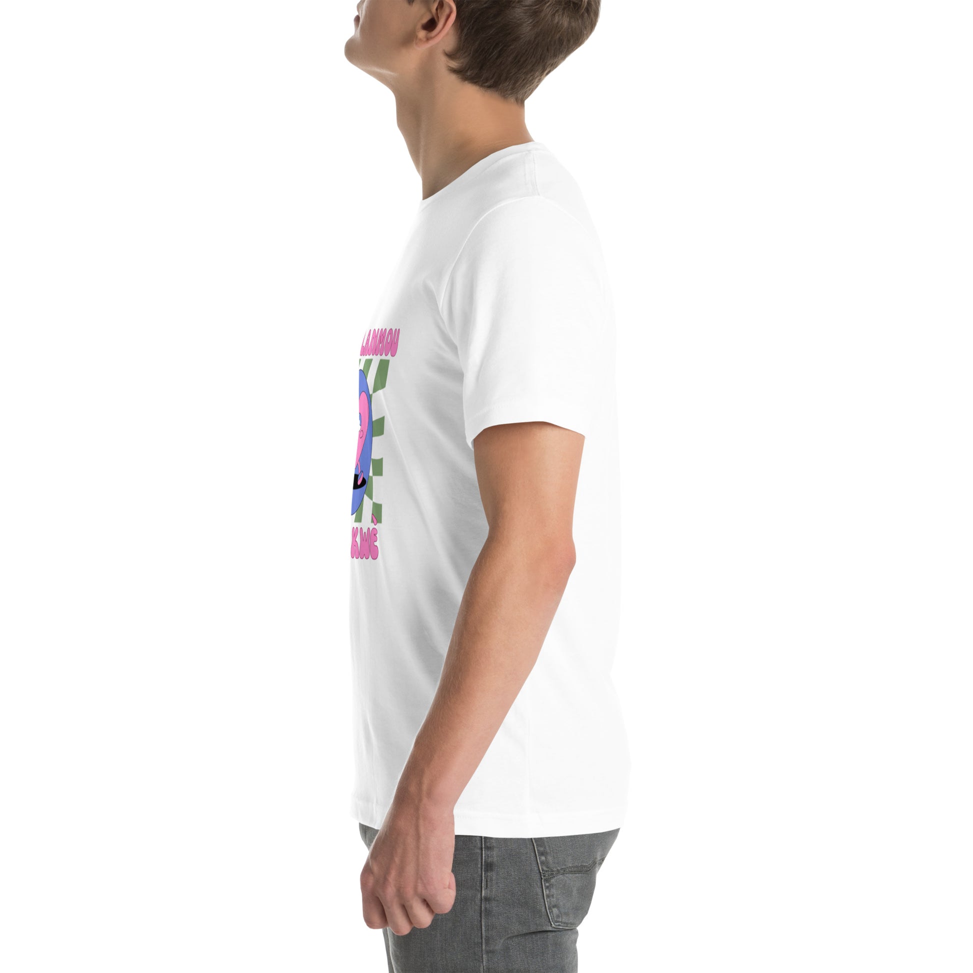 White man wearing a white Bella+Canvas 'Nan Lanmou Nou Kwe' unisex T-shirt (left side view) featuring a pink and blue abstract heart graphic with a smiley face and paint drip accents.