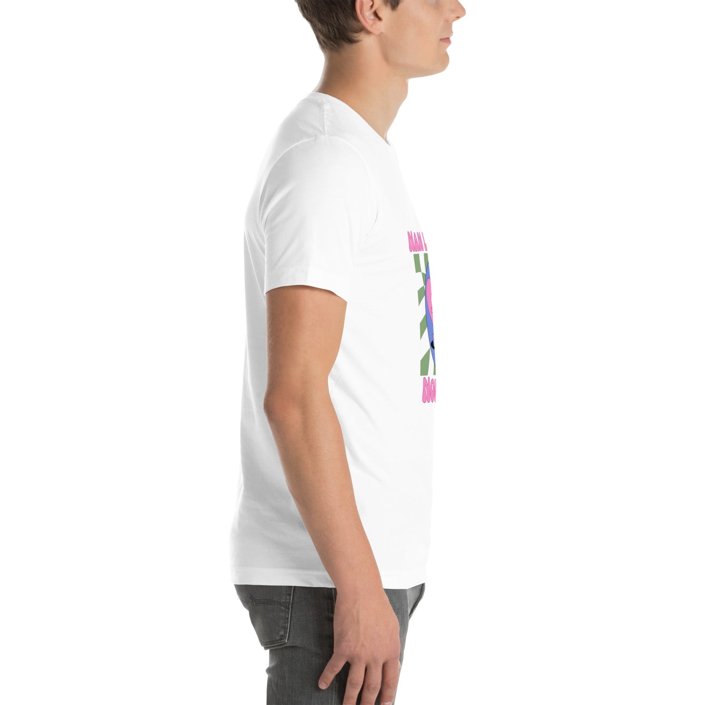 White man wearing a white Bella+Canvas 'Nan Lanmou Nou Kwe' unisex T-shirt (right side view) featuring a pink and blue abstract heart graphic with a smiley face and paint drip accents.